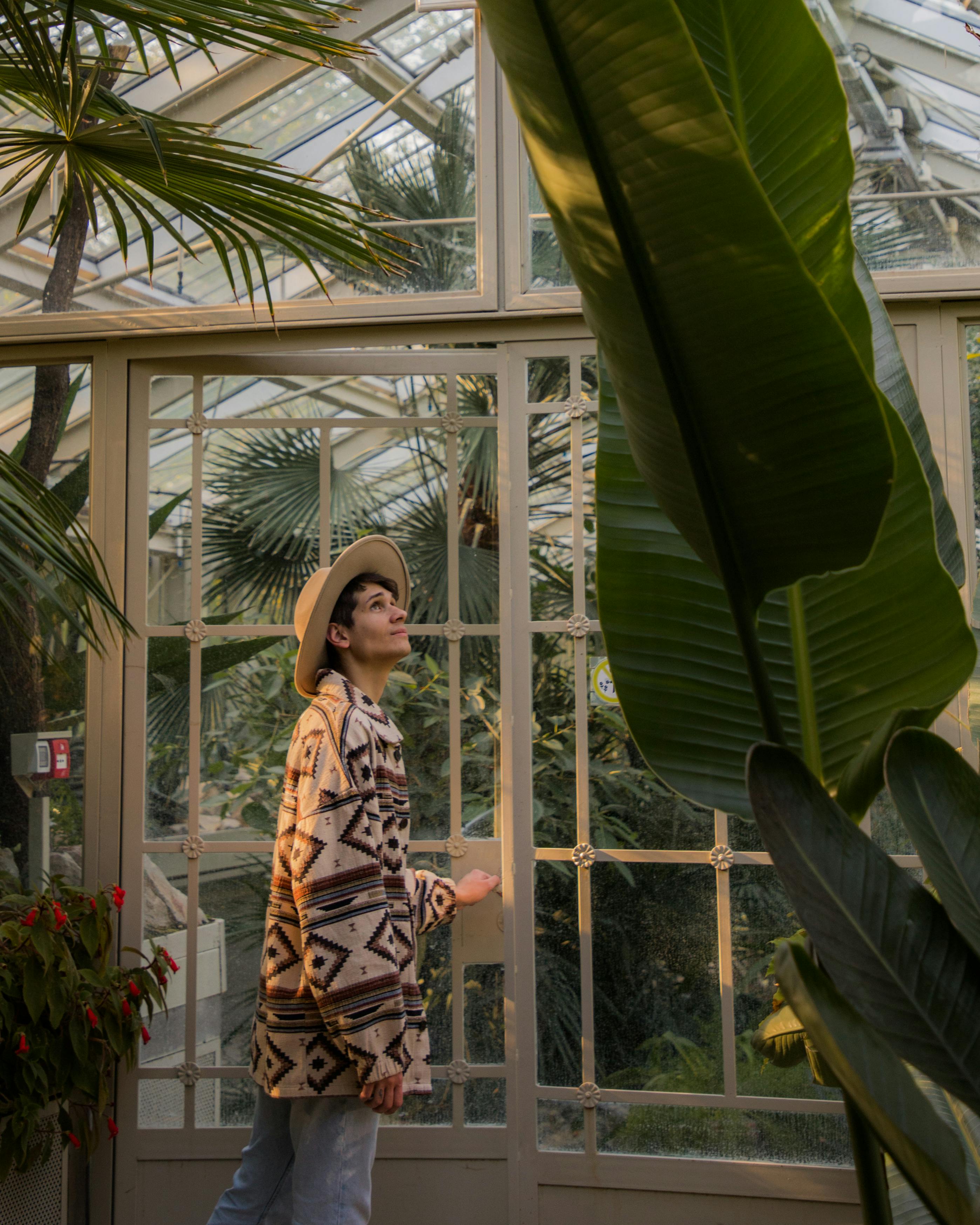 A young man in a stylish outfit explores a glasshouse botanical garden in Belgrade, Serbia.
