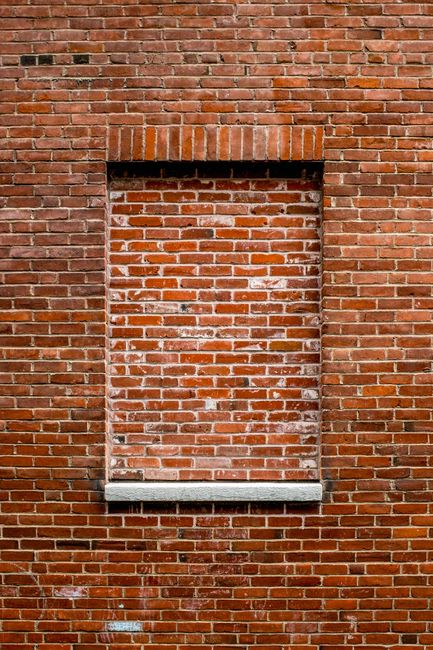 A vertical shot of a red brick wall with a sealed window frame in Boise, Idaho, capturing urban architecture.