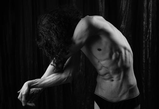 Black and white artistic shot of a muscular man stretching with dramatic lighting.