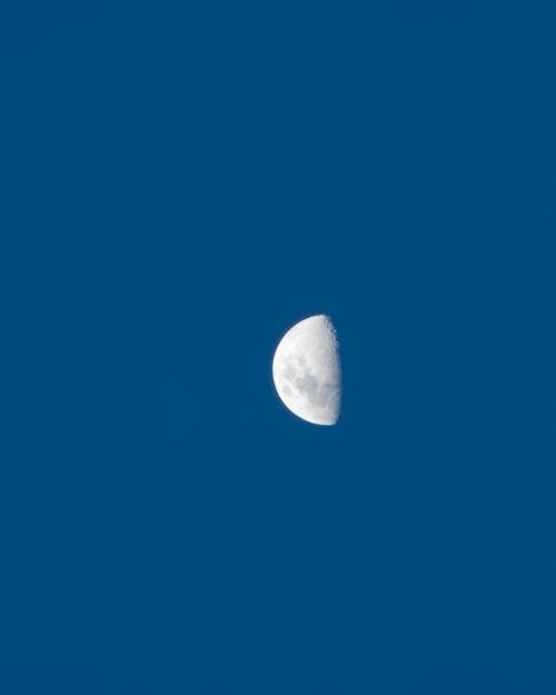 A white moon is seen in a blue sky