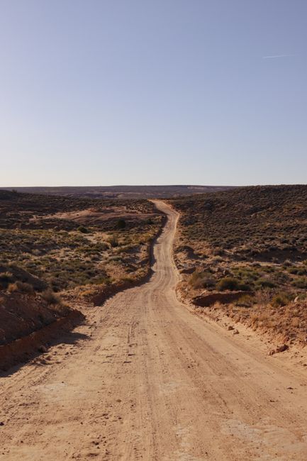 A picturesque dirt road winding through Escalante, Utah's arid and rugged terrain under a clear blue sky.