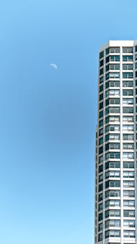 Modern skyscraper against a clear blue sky with a visible crescent moon.