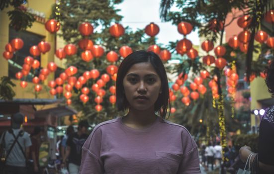 在城市环境中，一位年轻亚洲女性头顶挂着发光的灯笼