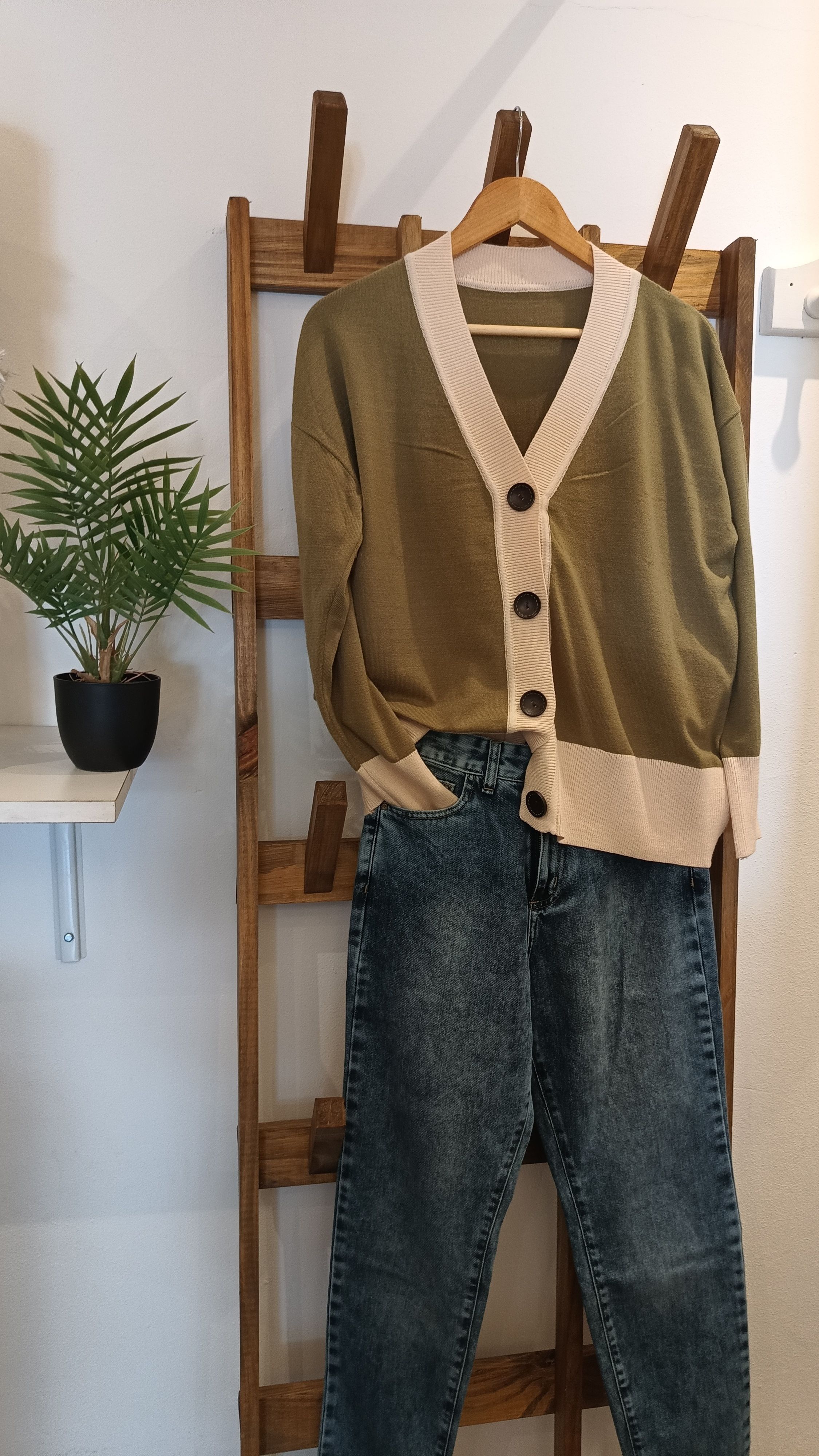 Fashionable cardigan and jeans on a wooden rack with a plant beside.