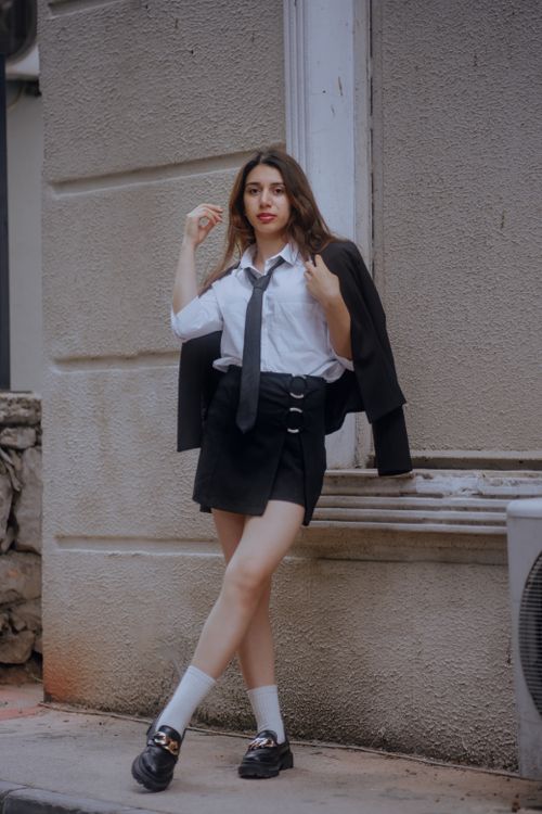 Free Stylish woman in black skirt and jacket poses against urban wall. Stock Photo