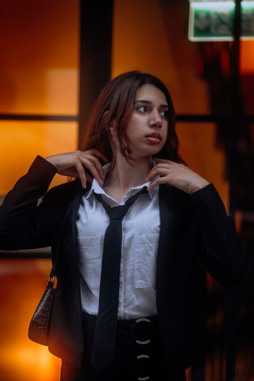 Free Portrait of a woman adjusting her tie, dressed in a formal suit with a contemplative expression. Stock Photo