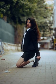 Woman in a stylish suit jacket kneeling on a city street showcasing urban fashion.