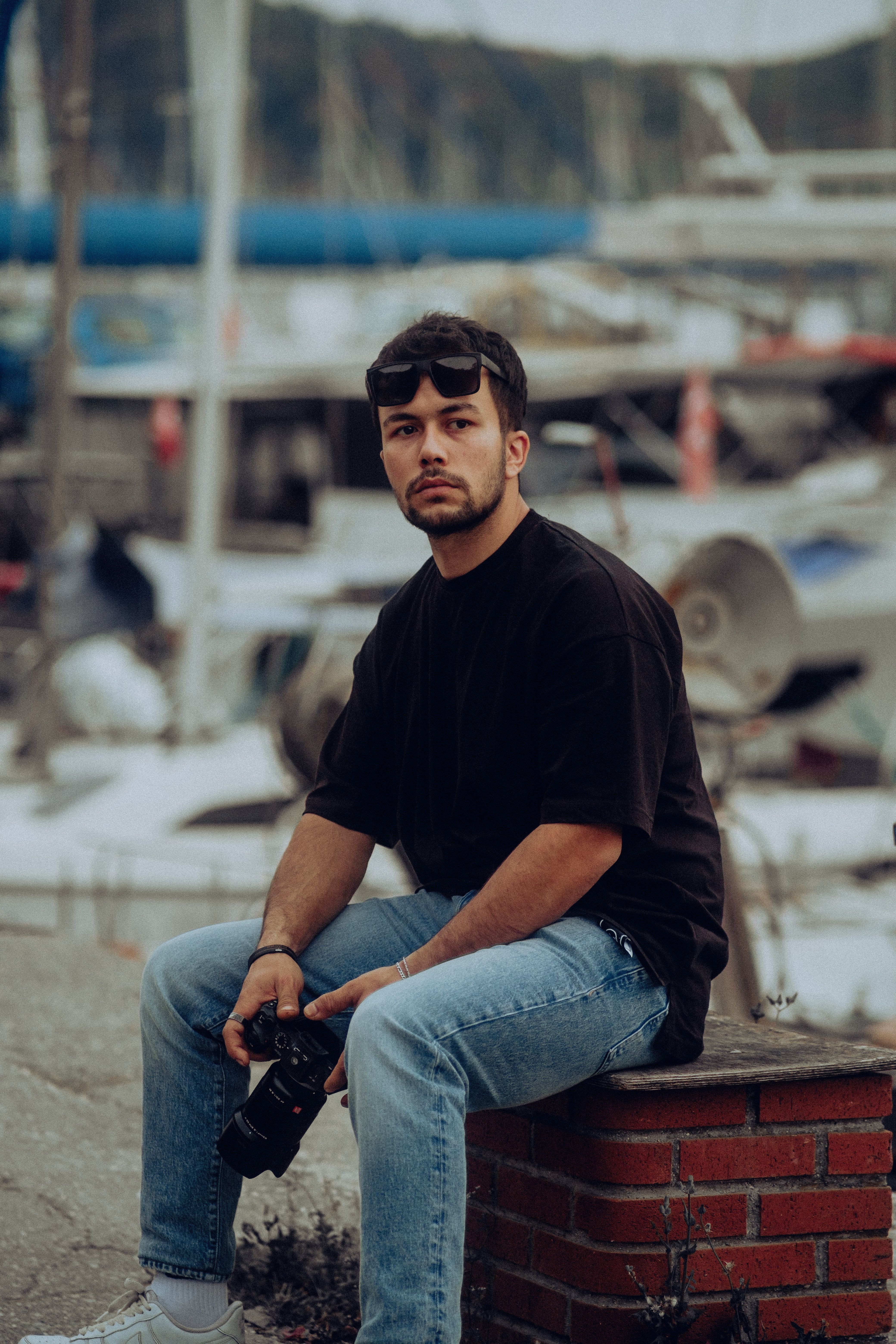 Stylish man in a black t-shirt and jeans sitting by the marina holding a camera