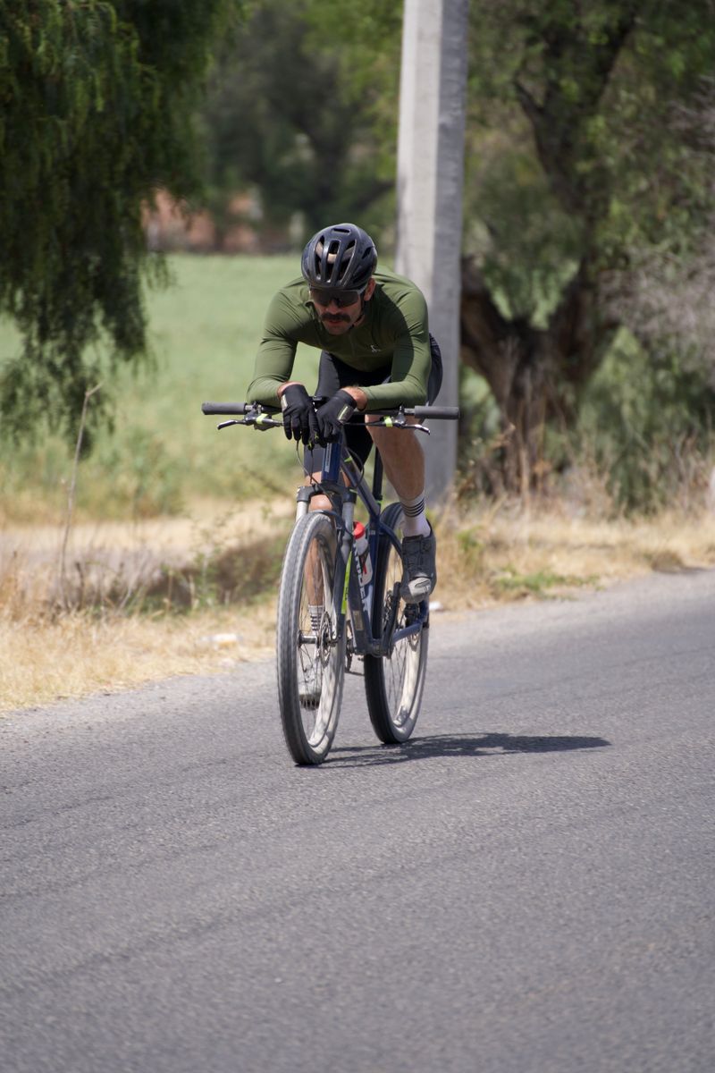 Focused cyclist riding a bicycle on a rural road surrounded by nature, showcasing active lifestyle.