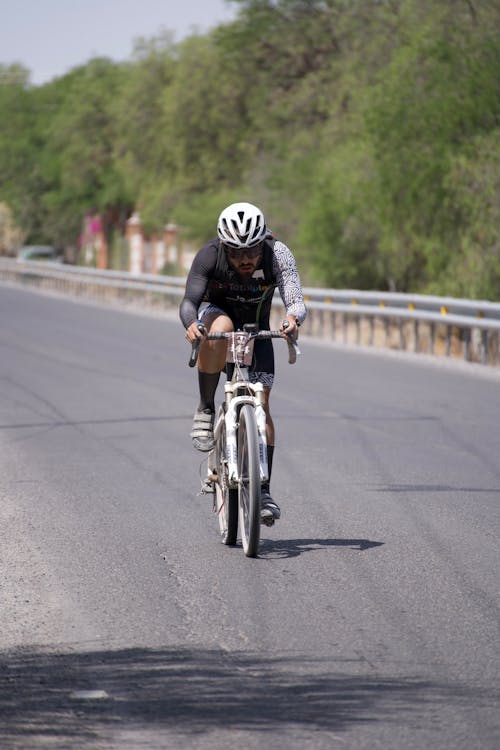 Man in White Helmet Riding a Bicycle on a Road