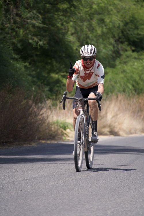 Free Smiling cyclist in helmet giving thumbs up while biking on a sunny rural road. Stock Photo