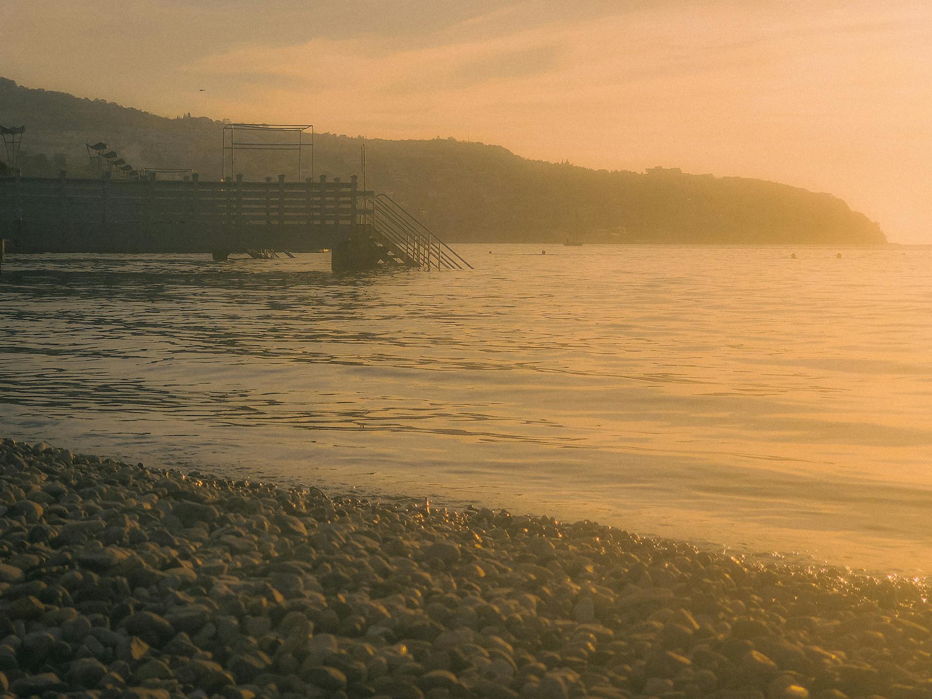 Tranquil sunset view of Koper coastline with pebbles, calm sea, and boardwalk in Slovenia.