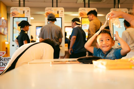 Smiling boy playing with a menu in a fast food restaurant. Lively atmosphere with people ordering.