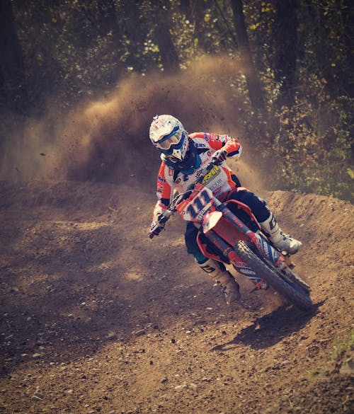 Homem De Macacão De Motocross Branco E Laranja Pilotando Sua Moto Suja De Motocross Durante O Dia