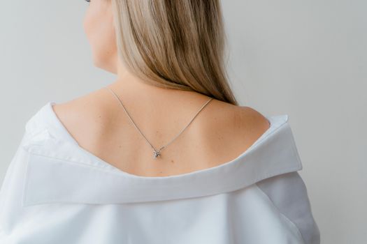 Back view of blonde woman wearing a necklace and white shirt, exuding elegance and simplicity.