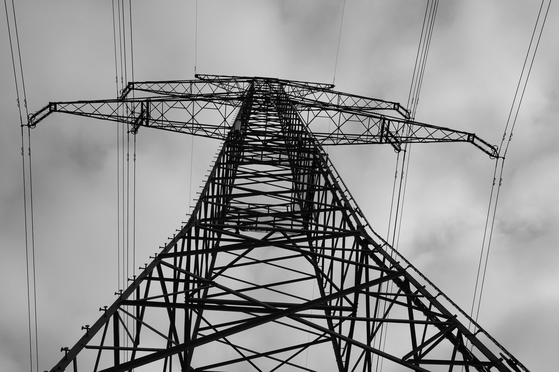 Black and white view of a power transmission tower against a cloudy sky, emphasizing structure.