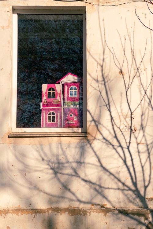 Free A vibrant dollhouse is reflected in a window, surrounded by tree shadows on the wall. Stock Photo