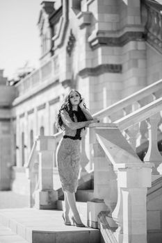 Stylish woman in dress posing on classic staircase in urban architecture.