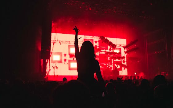 Silhouette of a woman raising her arm in a vibrant music festival with red lighting.