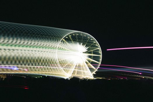 Blurred motion of an illuminated Ferris wheel captured at night with long exposure.