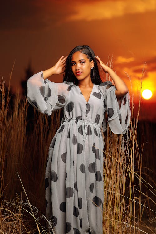A woman in a polka dot dress poses for a photo at sunset