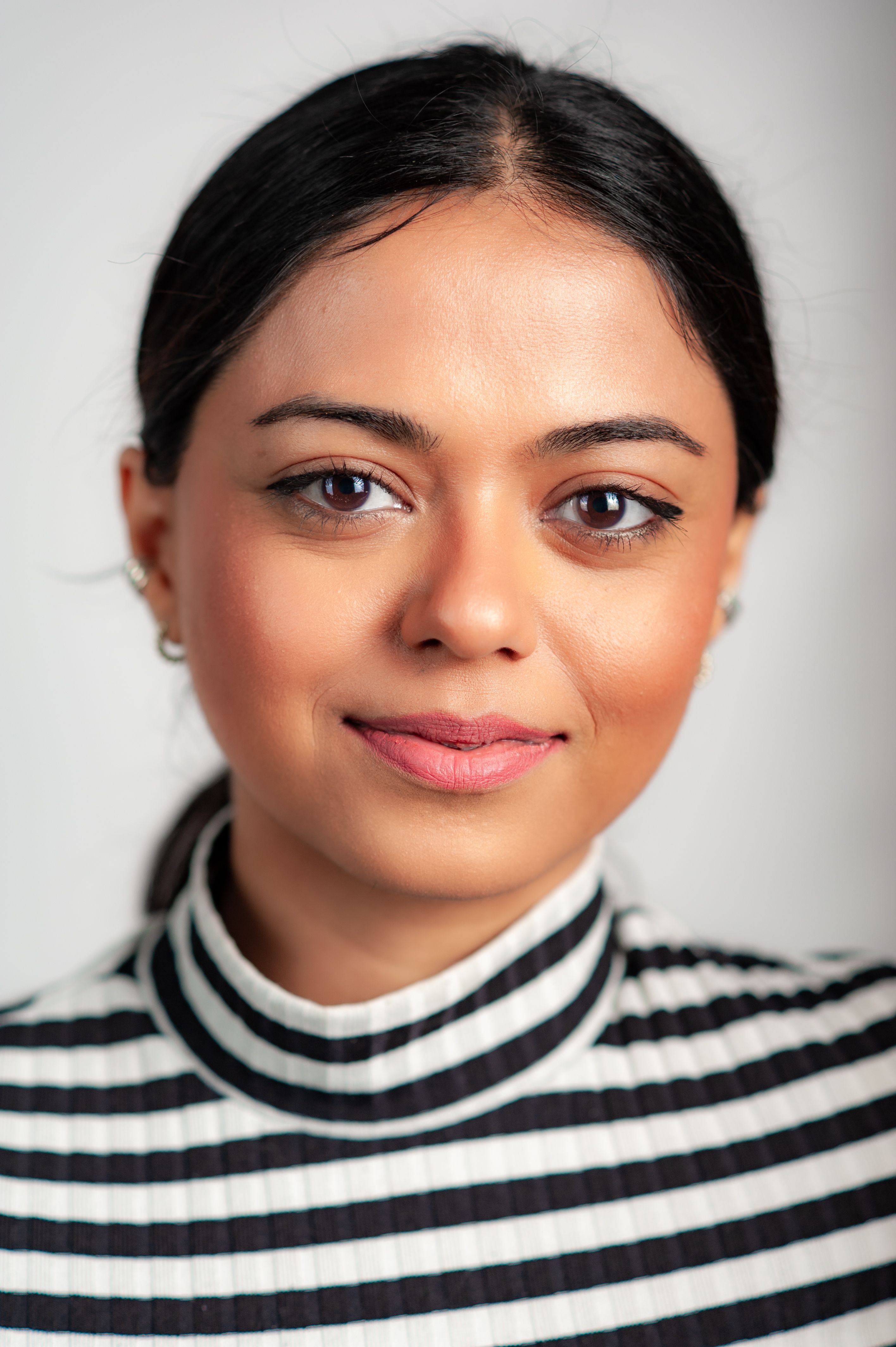 Close-up portrait of a woman with a confident expression, wearing a striped blouse on a white background.