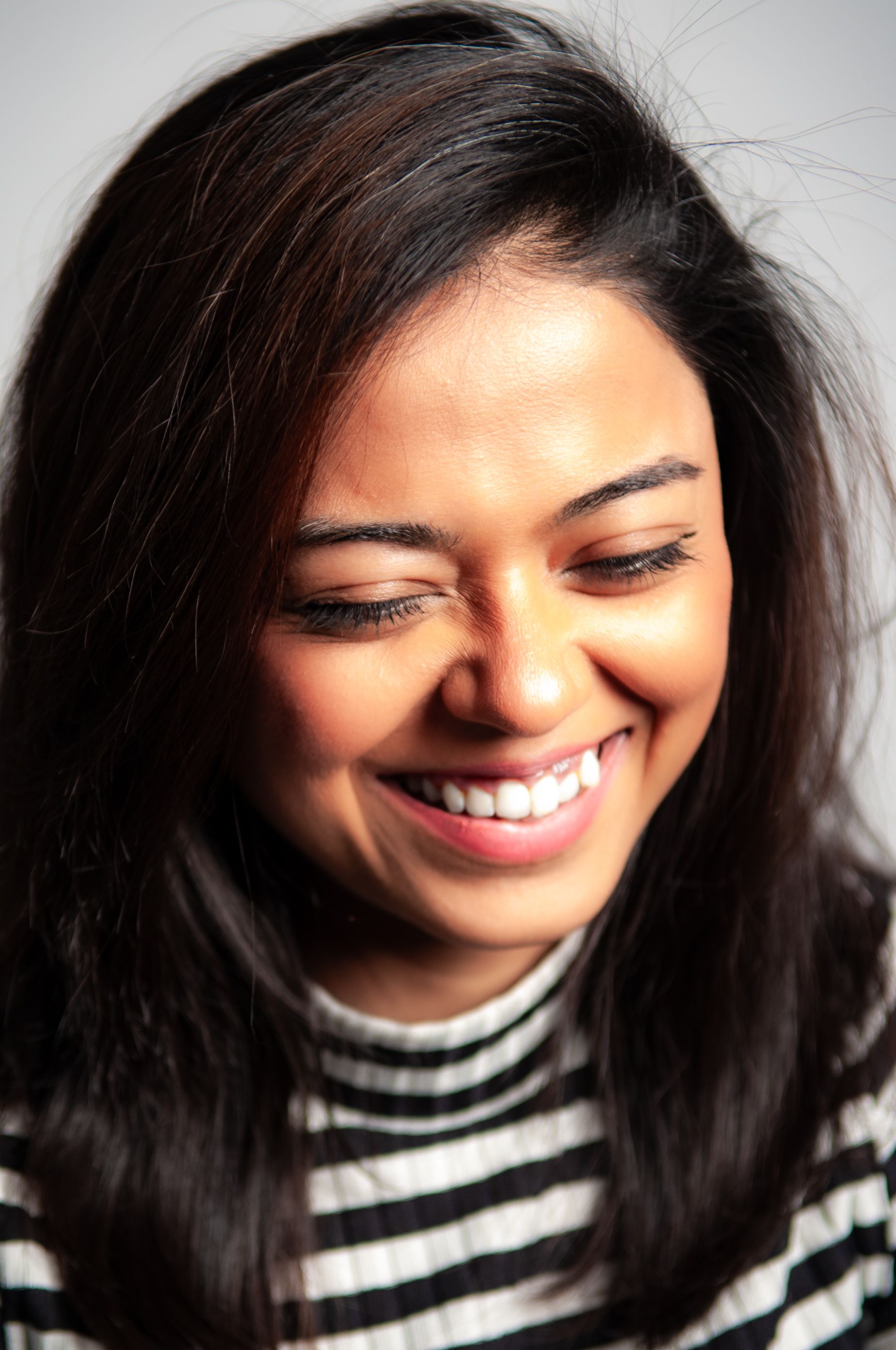 Close-up portrait of a smiling woman in a striped sweater, exuding joy.