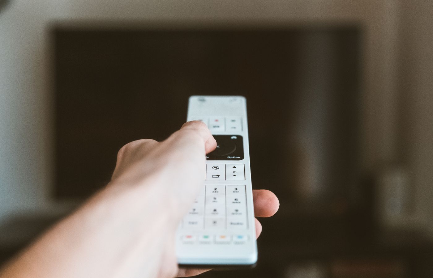 Close-up of a hand using a remote control to operate a television indoors.