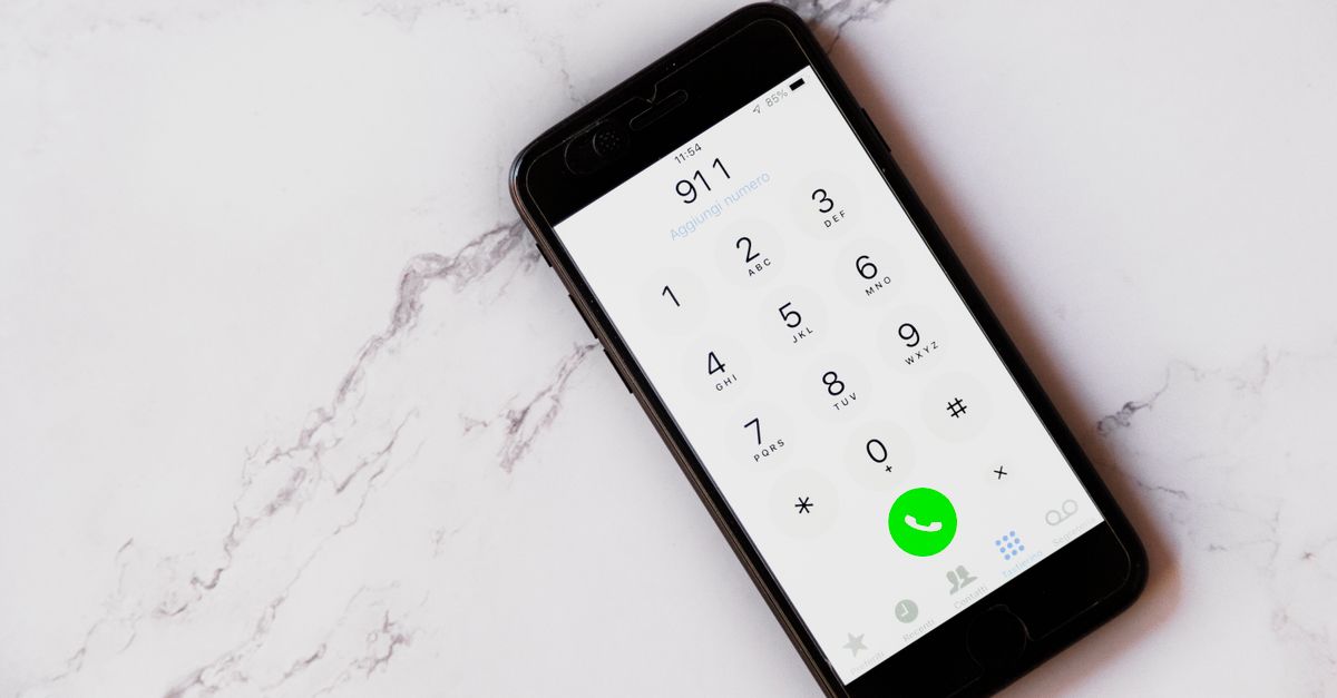 Close-up of a smartphone displaying the emergency number 911 on a white marble surface.