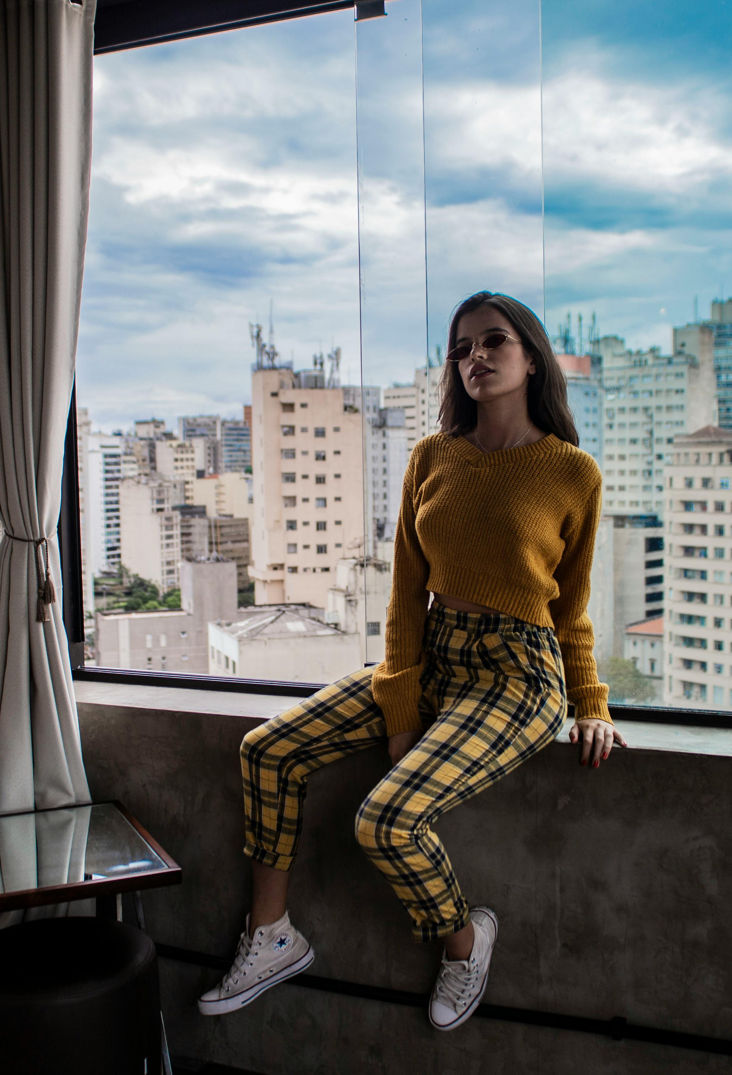 一位穿着休闲装的时尚年轻女子坐在窗前，俯瞰着城市天际线