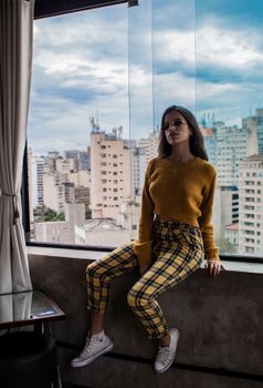 一位穿着休闲装的时尚年轻女子坐在窗前，俯瞰着城市天际线