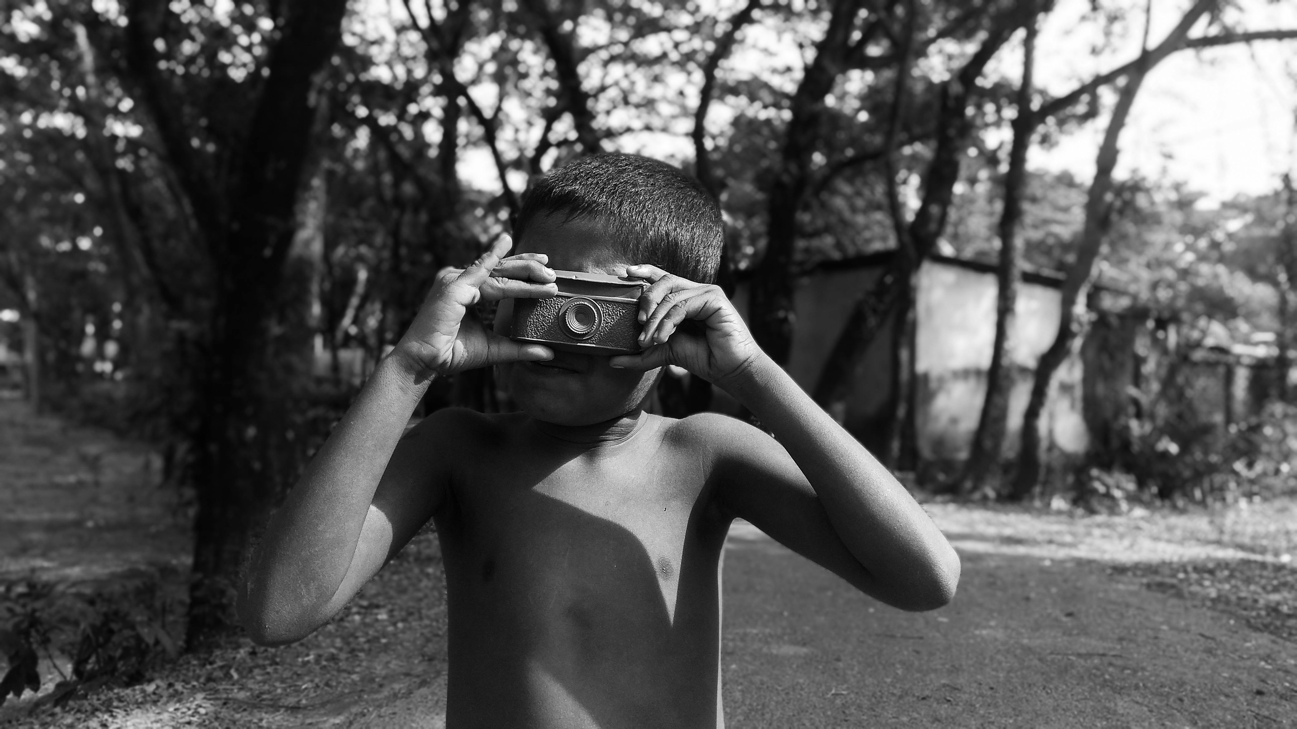 Young boy in Bangladesh enjoying outdoor photography with a toy camera.