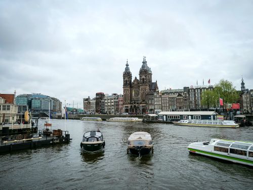 Free Capture of Amsterdam's Basilica of Saint Nicholas with boats on the canal under a cloudy sky. Stock Photo