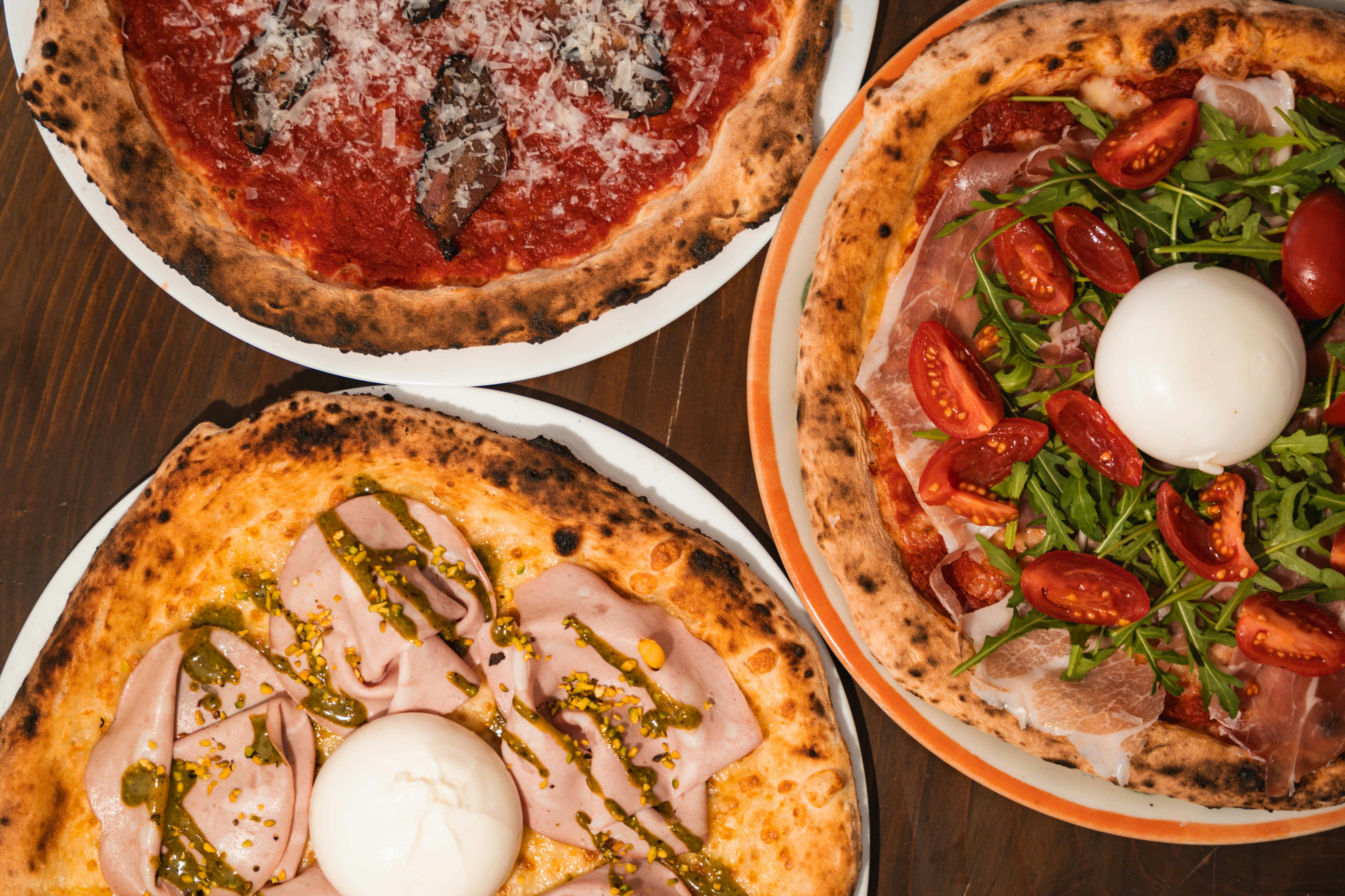 A close-up of various Italian pizzas with gourmet toppings, captured in an indoor Milan pizzeria.