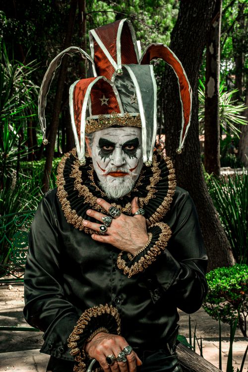 Free A man in an elaborate jester costume with makeup sitting outdoors in a park. Stock Photo