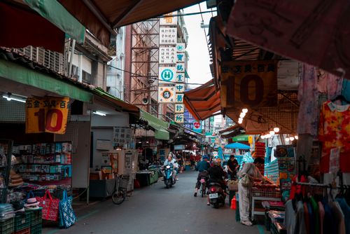 Free A lively street market scene with people shopping, scooters, and colorful stalls. Stock Photo