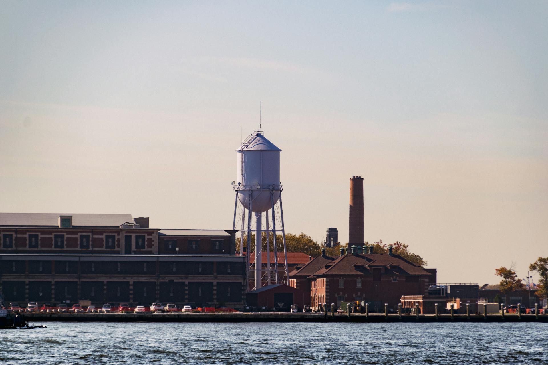 Water tower located by the water with surrounding factory buildings at sunset.