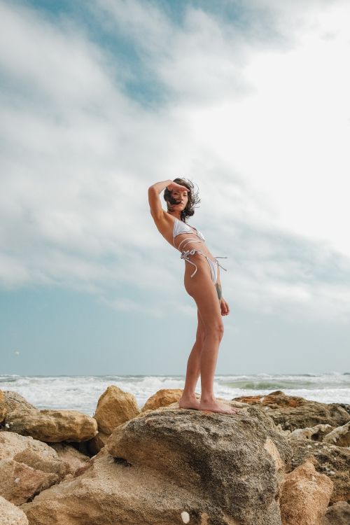 Free A woman poses confidently on rocks by the ocean, embracing the summer vibe. Stock Photo