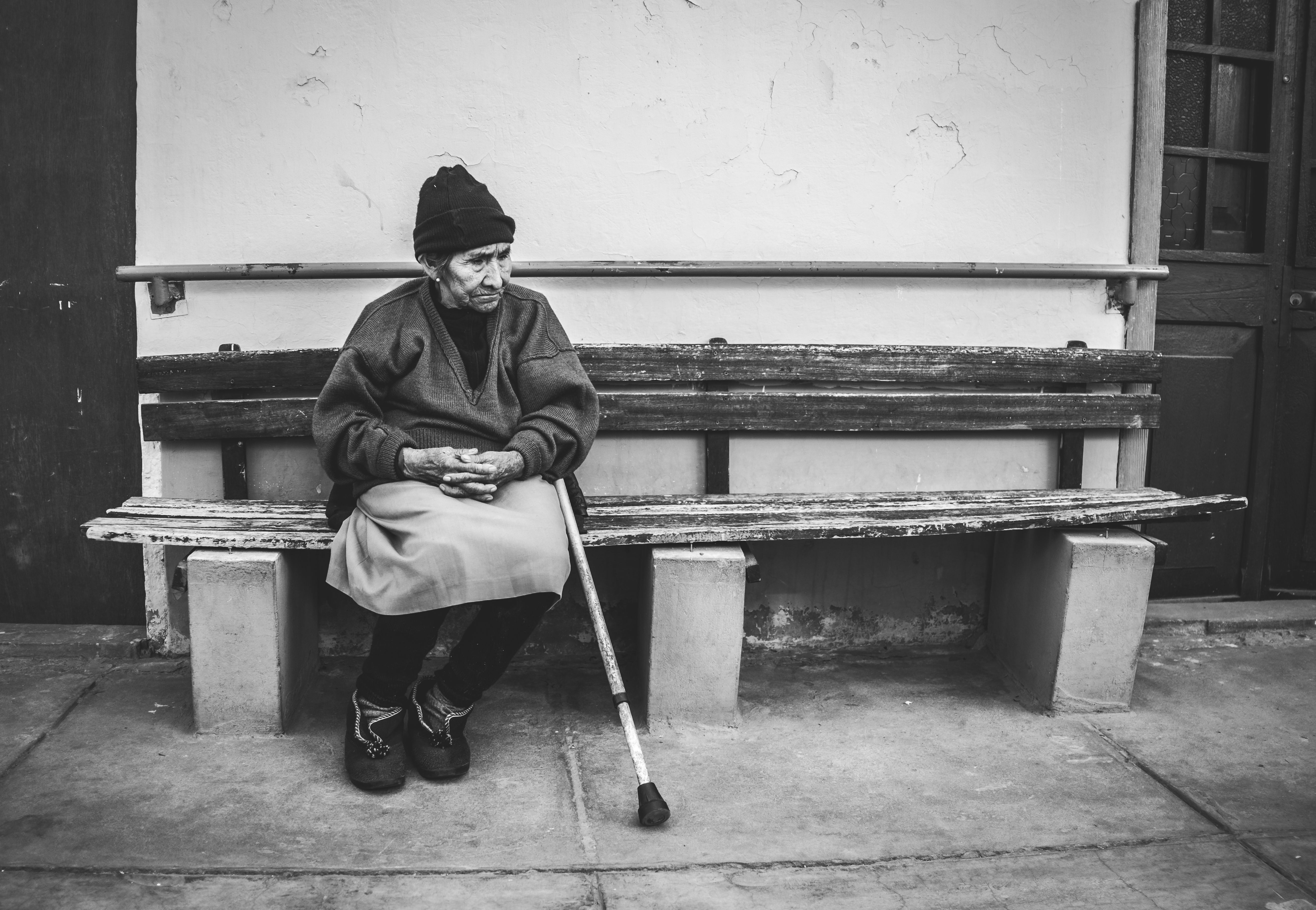 Black and white photo of an elderly woman sitting on a bench with expression of contemplation.