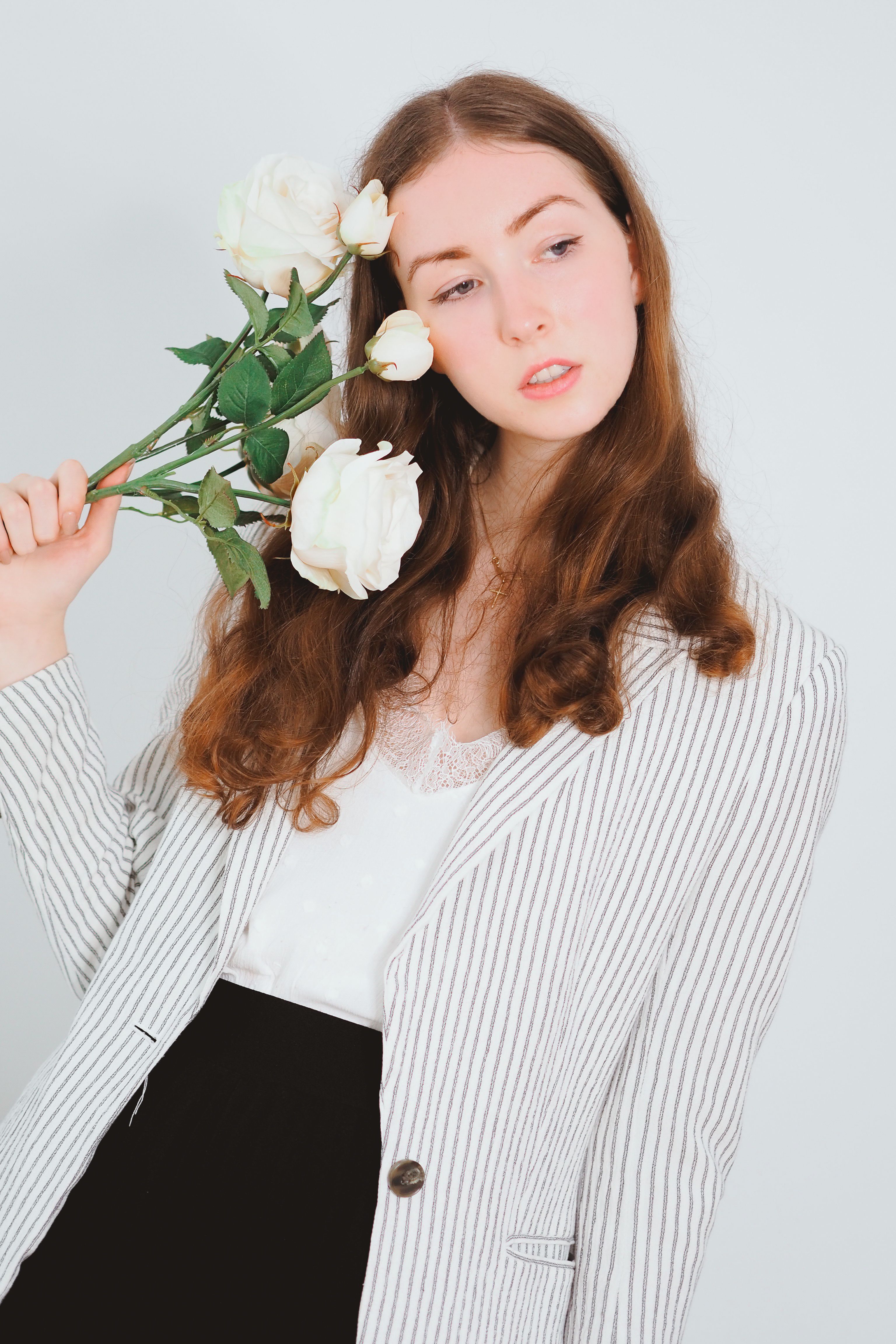 Stylish woman posing in a striped blazer holding roses, embodying elegance and fashion.