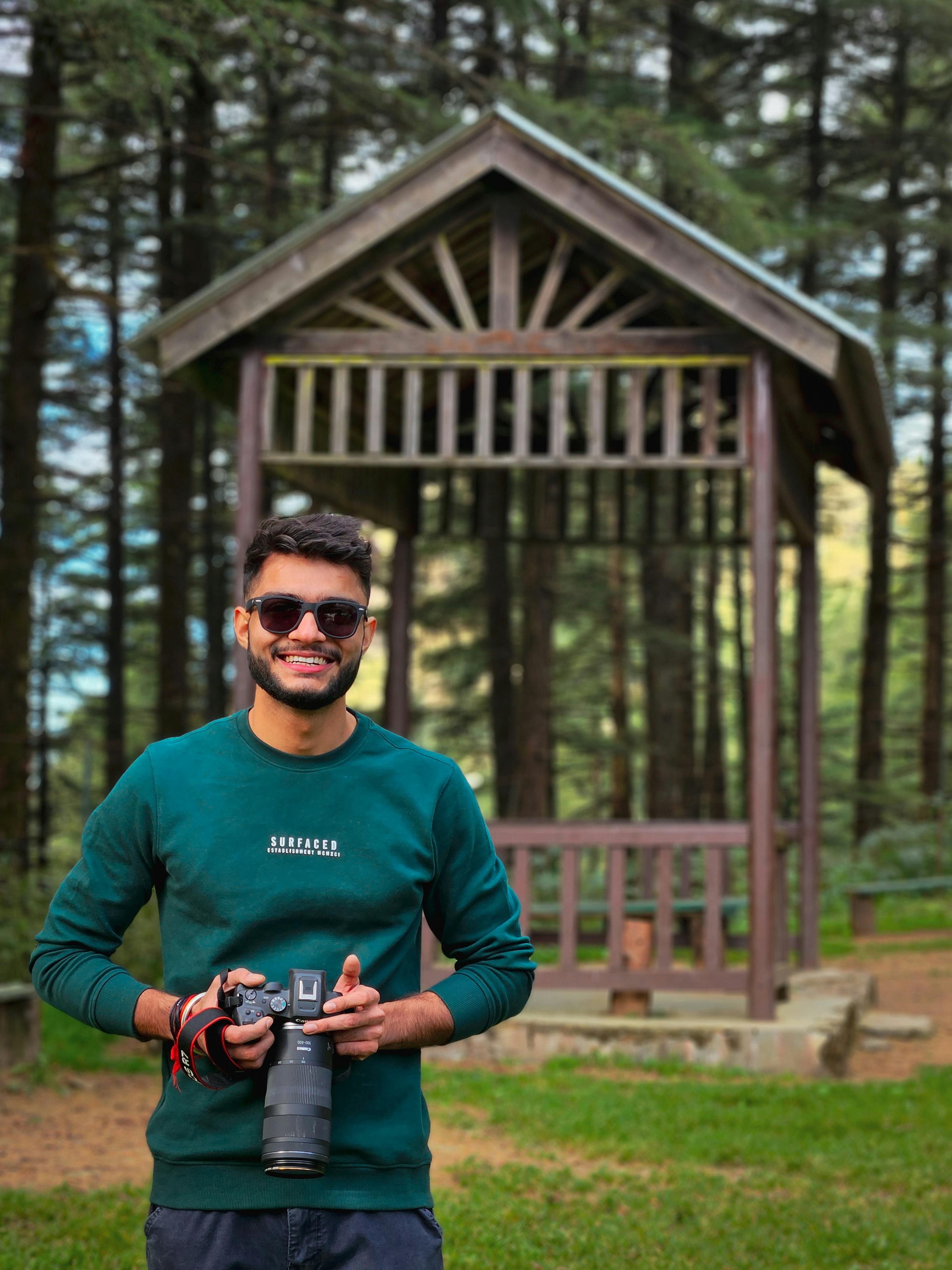 A smiling man with a camera in a lush forest setting in Dhanaulti, India. Perfect day for photography.