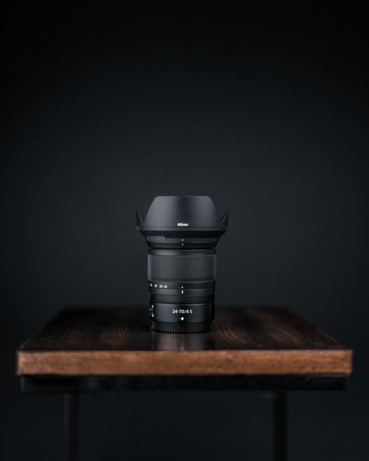 Close-up of a black camera lens on a wooden table against a dark background.