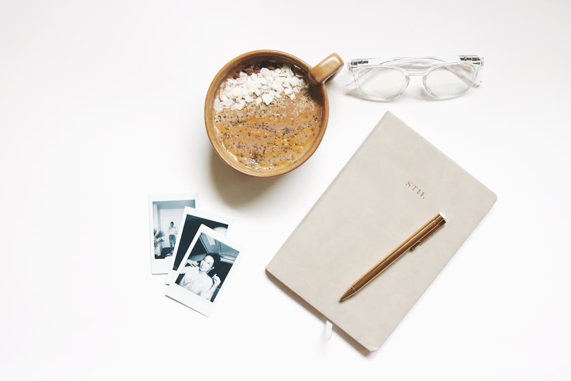 Free Brown Ceramic Cup Beside Notebook and Pen Stock Photo