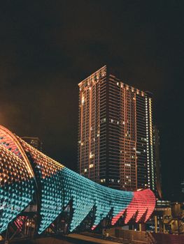 Illuminated Saloma Link bridge in Kuala Lumpur against skyscraper backdrop at night.