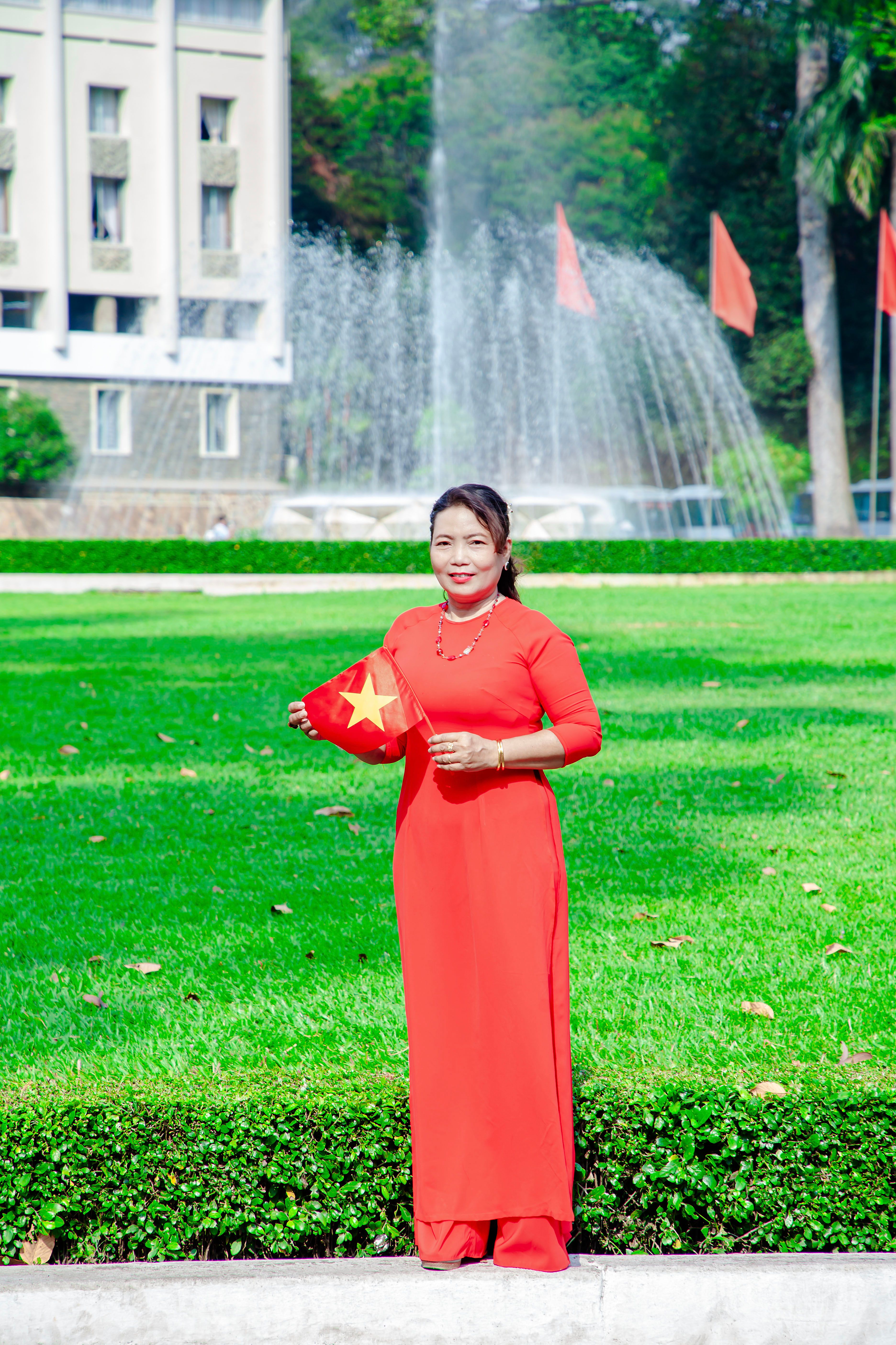 A Vietnamese woman in a red traditional dress holds a flag outdoors, symbolizing national pride.