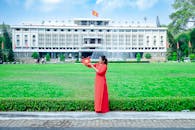 Woman in Red Traditional Ao Dai Posing in Front of Independence Palace with Vietnamese Flag