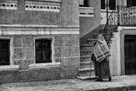 一位老妇人拄着拐杖走过一座乡村城市建筑，捕捉着街头生活的永恒瞬间