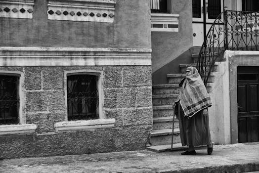 一位老妇人拄着拐杖走过一座乡村城市建筑，捕捉着街头生活的永恒瞬间