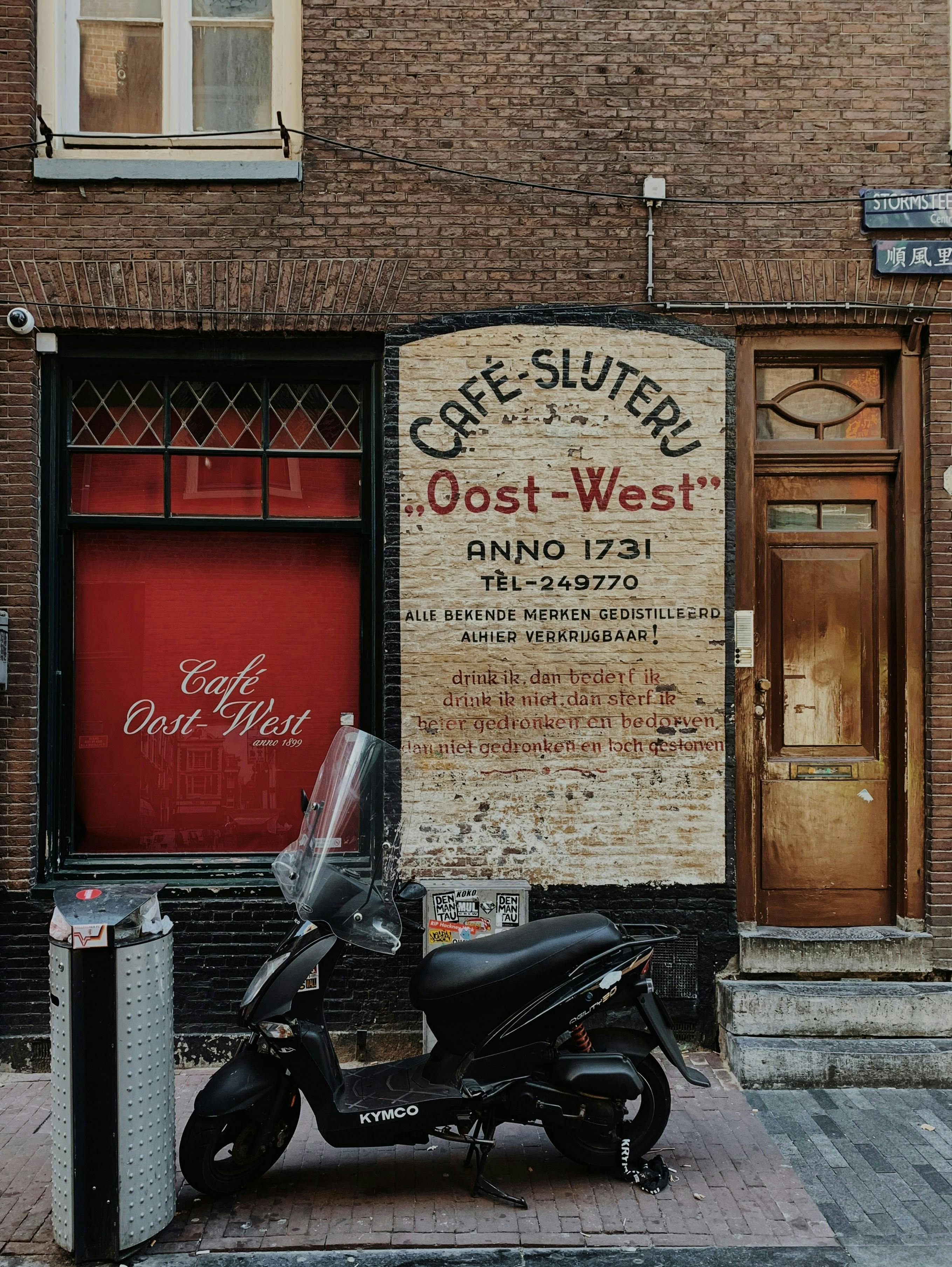 Historic café facade in Amsterdam featuring a parked scooter and vintage signage.