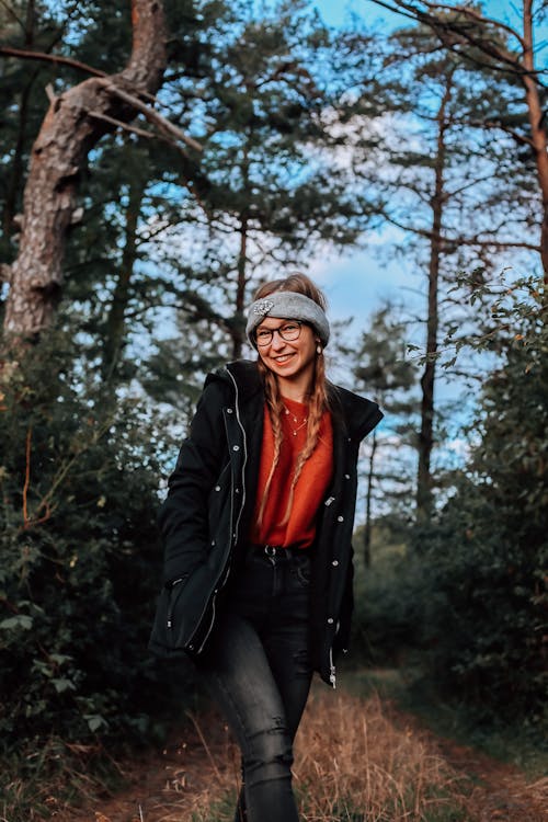 A woman in a black jacket and jeans standing in the woods